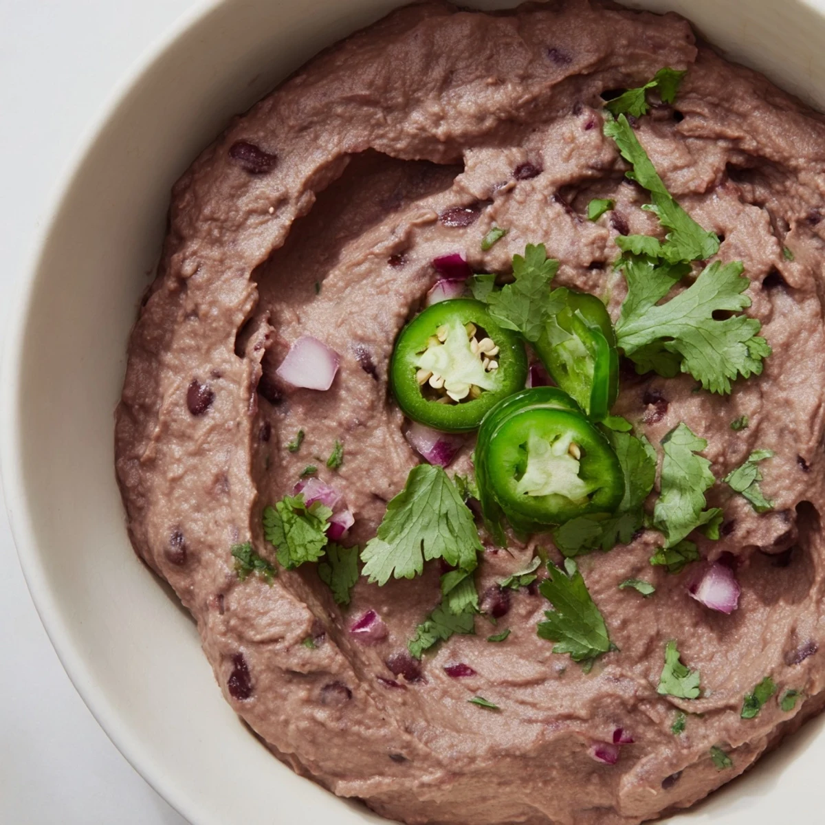 Vibrant, creamy Spicy Black Bean Dip in a bowl, garnished with fresh cilantro, lime wedges, and sliced jalapeños for a bold, smoky flavor.