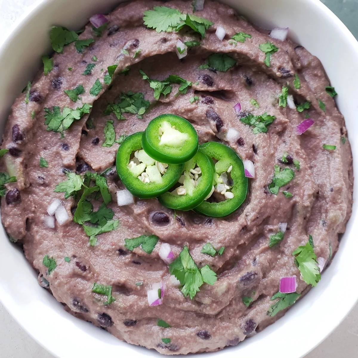 A vibrant bowl of Spicy Black Bean Dip, topped with crumbled feta, cilantro, and jalapeños, perfect for party appetizers or taco night.