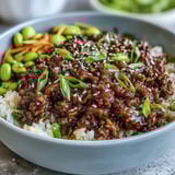 A prepared Korean Ground Beef Bowl featuring edamame, cucumber, and carrots, garnished with green onions and sesame seeds.