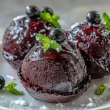 Scoops of homemade Black Currant Sorbet served on a chilled ceramic dish, garnished with a fresh sprig of mint for a vibrant finish.