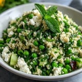 A vibrant bowl of Spring Pea and Mint Couscous Salad garnished with fresh herbs and lemon, ready to serve.