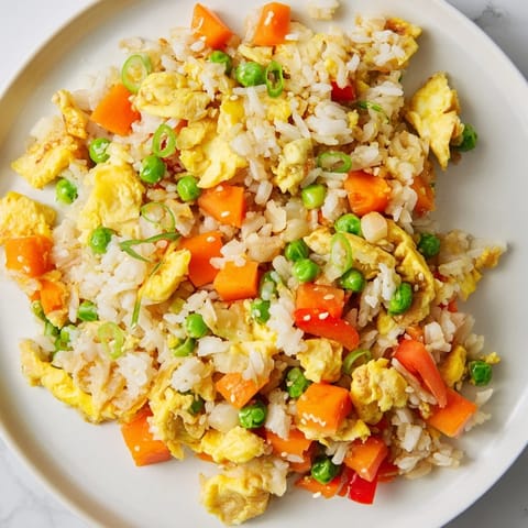 A close-up of steaming Egg Fried Rice, garnished with fresh scallions and served alongside chopsticks.  