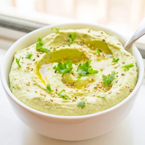 Fresh green Edamame Hummus blended smooth with tahini and lemon, drizzled with olive oil and sprinkled with sesame seeds, paired with colorful veggie sticks.  