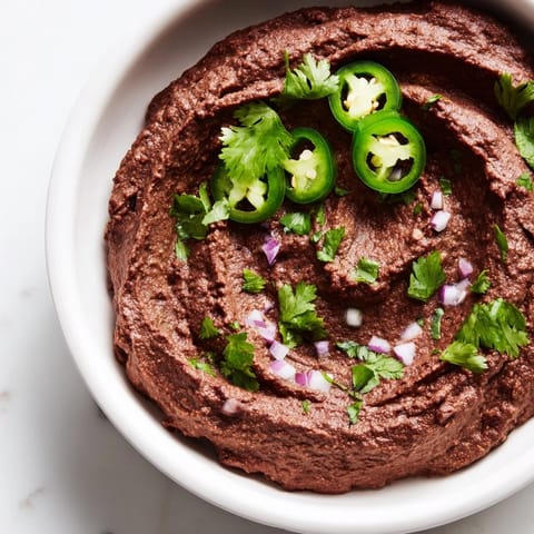 A close-up of freshly blended Spicy Black Bean Dip with a smooth texture, served with crunchy tortilla chips for dipping on a rustic table.