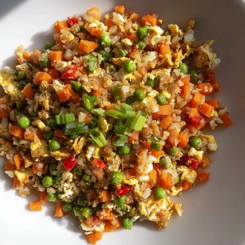 Steaming Cauliflower Fried Rice piled high, garnished with sliced green onions and a drizzle of toasted sesame oil.  