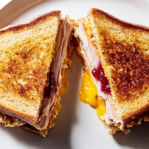 A close-up view of Smoked Turkey Grilled Cheese showing melted cheese pull from the layered turkey and tangy cranberry sauce.  