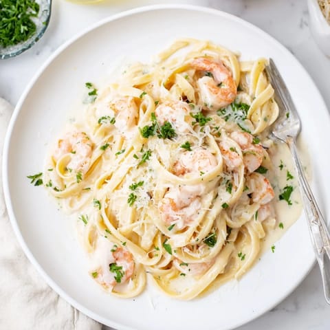 A close-up view of Creamy Garlic Shrimp Pasta reveals rich, velvety sauce clinging to al dente pasta and plump pink shrimp.  