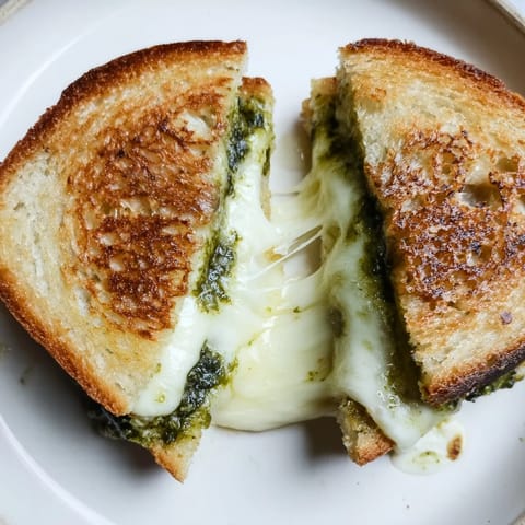 A close-up of sourdough pesto grilled cheese sandwich on a plate, paired with a fresh side salad.