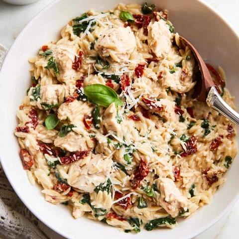 Tuscan Chicken Orzo served hot, garnished with fresh basil and extra Parmesan, on a rustic wooden table.