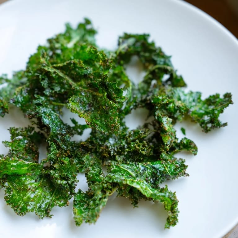 A close-up of perfectly crisp, seasoned kale chips fresh from the oven, ideal for a vegan afternoon treat.