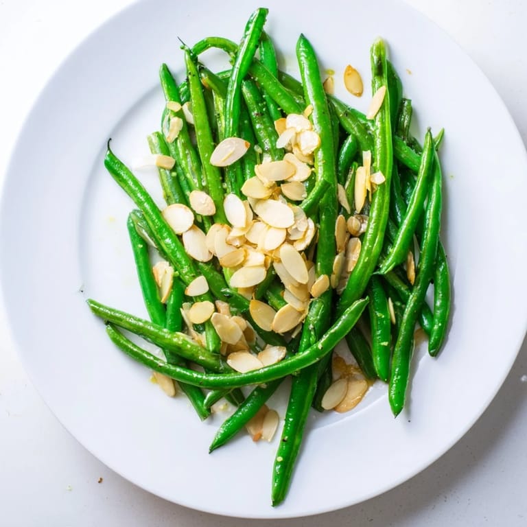 Fresh, tender sautéed green beans with garlic and almonds, tossed in a pan and sprinkled with toasted nuts.