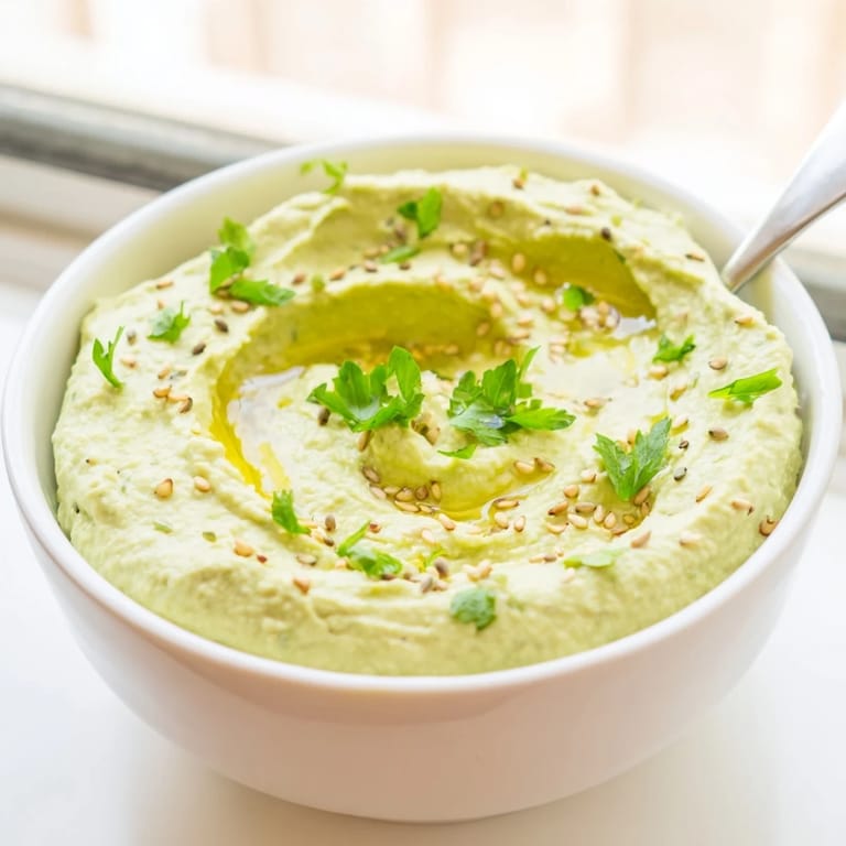 Fresh green Edamame Hummus blended smooth with tahini and lemon, drizzled with olive oil and sprinkled with sesame seeds, paired with colorful veggie sticks.  